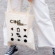 femme en pantalon blanc et basket converse noires sur route pavee qui porte un tote bag a la main avec les pictos et le nouveau logo du cinema le foyer de bourg argental pilat 42