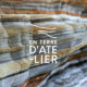 logo en terre d atelier blanc sur photo d une falaise avec aspect rayures de couleurs ocre gris et rouille